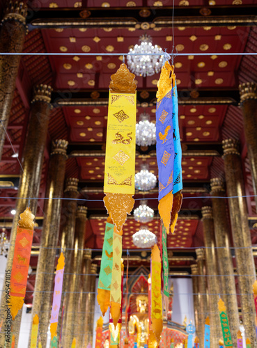 Colorful Thai religious flags hanging inside Buddhist temple. Traditional decorations symbolizing blessings, faith and spiritual harmony in sacred interior setting in Thailand.