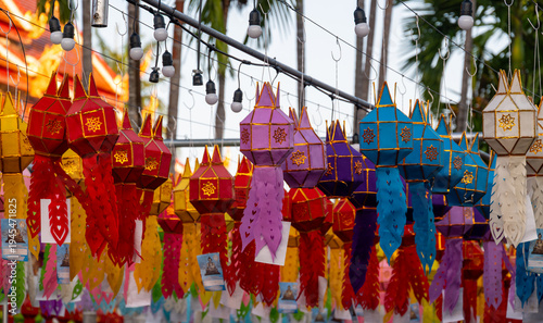 Colorful Buddhist prayer flags hanging from tree near temple in Thailand. Traditional decorations symbolizing blessings, peace and spiritual harmony fluttering gently in warm tropical air.