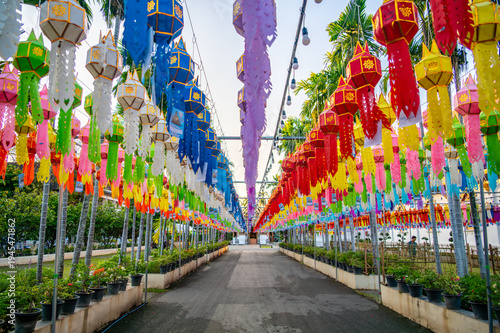 Colorful Buddhist prayer flags hanging from tree near temple in Thailand. Traditional decorations symbolizing blessings, peace and spiritual harmony fluttering gently in warm tropical air.