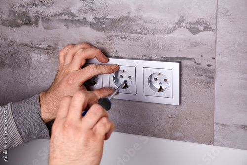Bild auf Leinwand An electrician installs an electrical outlet using a screwdriver on a wall cove