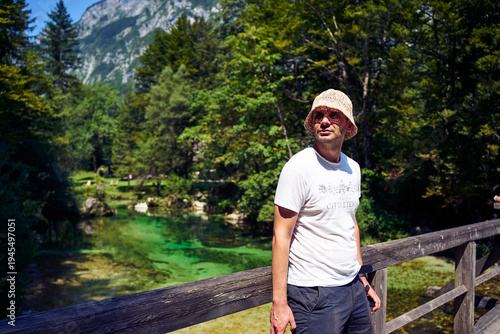  man in bucket hat standing by the crystal clear turquoise river in Slovenian Alps
