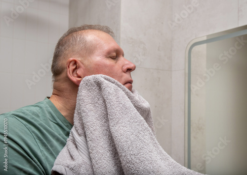Wallpaper Mural Mature man dries face with towel after washing in bathroom. Adult male wipes skin during morning hygiene routine. Everyday personal care moment inside modern home interior.. Torontodigital.ca