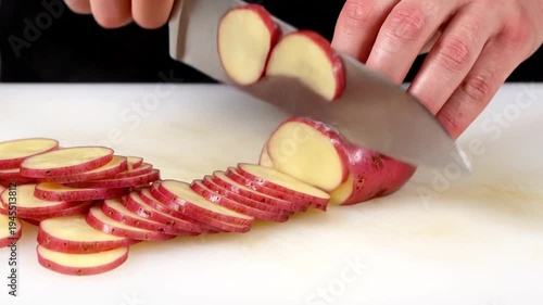 Hands slicing red potatoes on table.