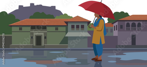 Indian woman holding a bright red umbrella standing on a flooded wet city street with water puddles during the heavy monsoon season near ancient historical houses.