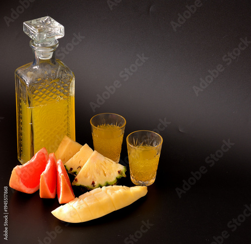 Photos Homemade fruit liqueur made from pineapple, mango, and grapefruit in a crystal glass against a black background