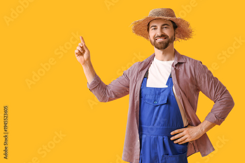 Young happy male farmer pointing at something on yellow background