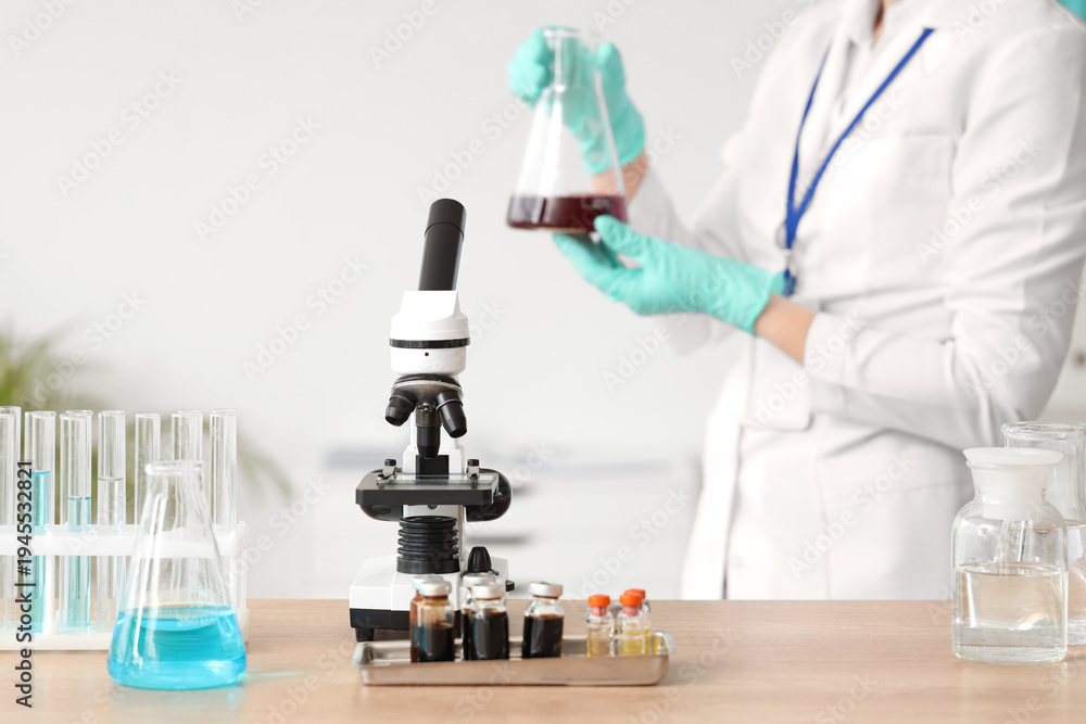 Fototapeta premium Female scientist with flask and microscope on table in laboratory