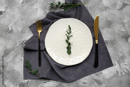 Beautiful table setting with golden cutlery and eucalyptus branches on grey grunge background