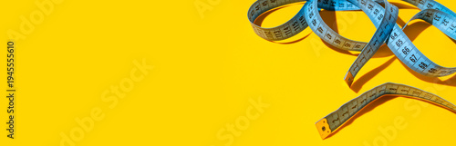 Blue measuring tape, centimeter on yellow background with sun shadow. Tape for tracking body measurements, sewing clothes. Minimalist concept for diet, weight loss, fitness. Flat lay top view