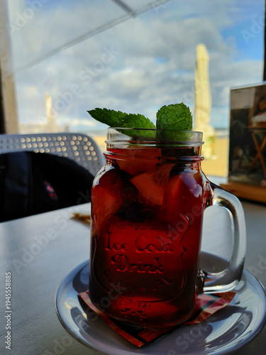 Close up of a red fruit drink in a glass jar with mint leaves on table