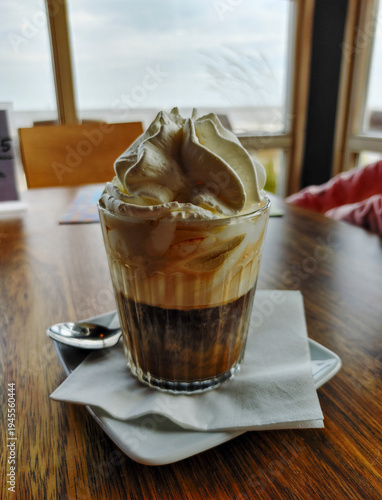 Coffee drink with whipped cream served in a glass on a wooden table