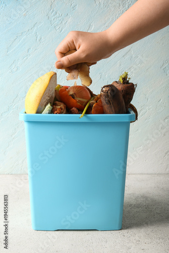 Foto Female hand putting potato peels into bucket with organic waste on white grunge table