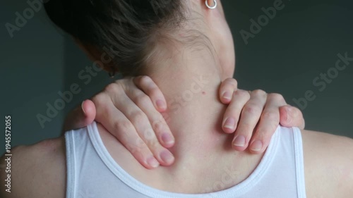 Woman in white tank top massaging her tired neck and tense shoulders, trying to relieve muscle stiffness, pain caused by overwork, stress, sedentary lifestyle. Woman massaging neck pain her shoulders