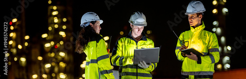 Petrochemical industry night engineer teamwork working on laptop Team of Petroleum in Glowing Workwear Collaborating oil refinery plant construction site at night