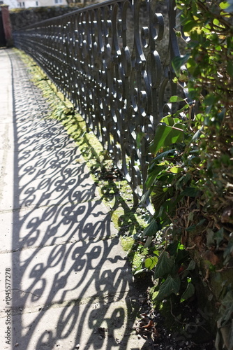 Ornamental fence casting decorative shadow pattern on sidewalk