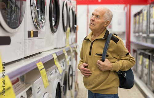 Bild auf Leinwand elderly man choosing washing machine in showroom of electrical appliance store
