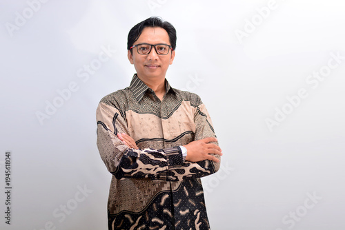 Portrait of a confident Indonesian businessman in traditional batik shirt standing with crossed arms against white background