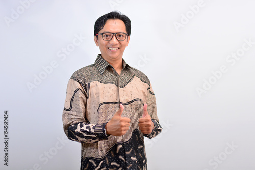 Happy Indonesian man wearing eyeglasses and batik shirt giving double thumbs up for recommendation