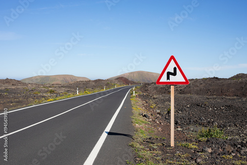 A straight, black, endless road with hills and mountains in the background. Spain, Lanzarote. A sign on the side of the road