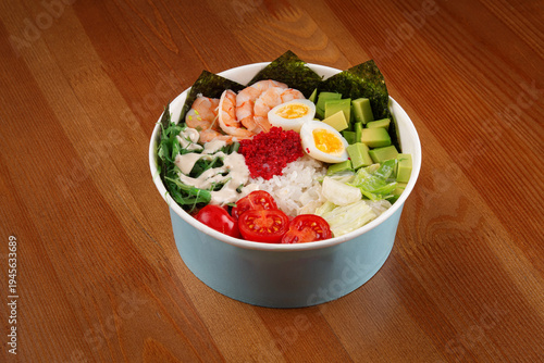 Fresh shrimp poke bowl with avocado, egg, seaweed salad, cherry tomatoes, rice and tobiko served on wooden table