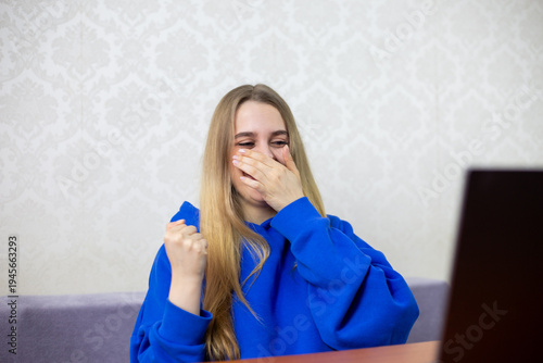 Εκτύπωση καμβά Blonde girl laughs uncontrollably at funny cartoon on laptop, covering mouth with hand