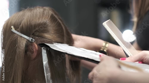 Professional hairdresser applying bleach to a section of hair using a brush and foil during a salon treatment