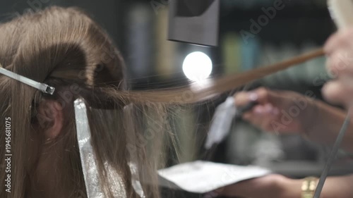Professional hairstylist applying hair dye to a female client using foil highlights technique