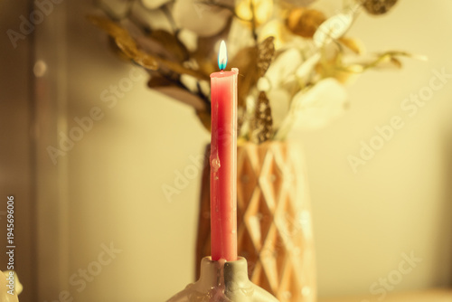 A single burning pink candle sits in a ceramic holder, creating a soft, warm glow. In the blurred background