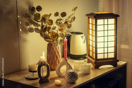 A cozy evening scene featuring a wooden table with glowing candles, a decorative vase with gold foliage, heart-shaped mugs, and an elegant Japanese-style wooden lamp, creating a warm atmosphere.