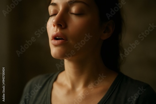 Woman focusing on breath, gently exhaling with eyes closed, embodying calm, relaxation and mindfulness in a serene studio moment of self care, stress relief and inner peace