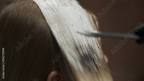 Hairstylist applying white dye mixture to hair roots with a tint brush in a salon