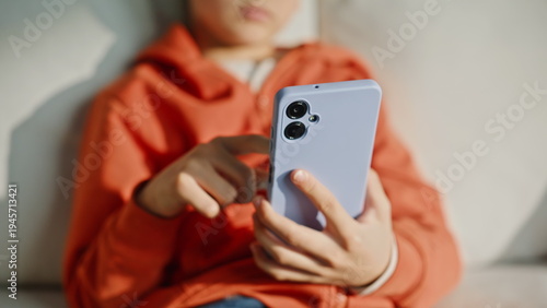 Kid hands scrolling mobile phone news feed sitting living room couch closeup. 