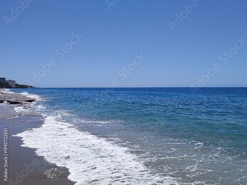 Coastline waves washing onto sandy shore under clear sky