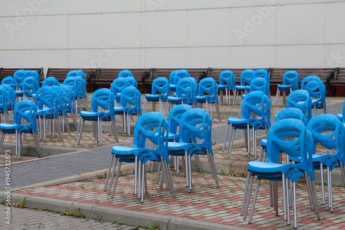 Rows of blue plastic chairs sit empty under a white building