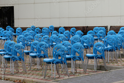 Rows of blue plastic chairs sit empty under a white building