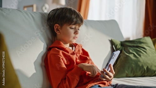 Relaxed boy browsing cellphone sitting home sofa closeup. Child scrolling phone