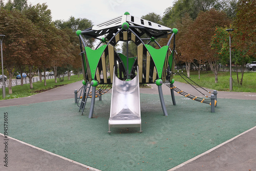 Green playground structure with metal slide and climbing gear