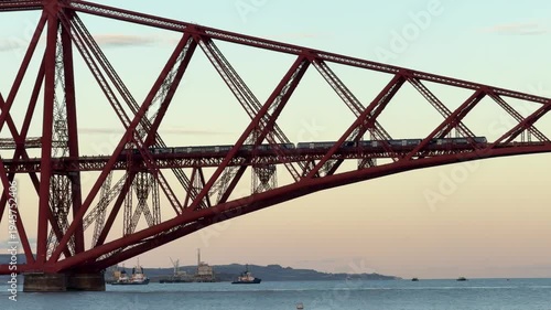 Train crossing historic Forth Bridge cantilever railway at golden hour, Edinburgh, Scotland