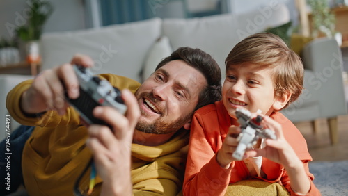 Smiling father taking picture cute little son playing lego lying floor closeup.