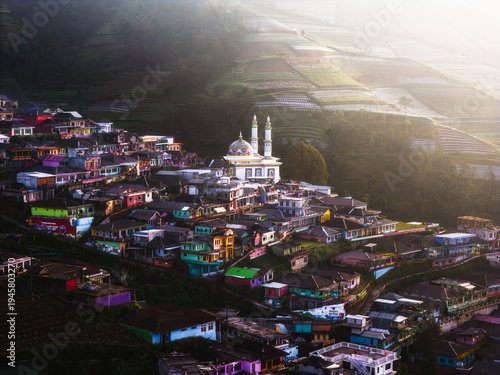 Aerial view of a mosque standing tall amidst a vibrant village, nestled against terraced hillsides touched by the warm glow of sunlight, Nepal van Java, Jawa Tengah, Indonesia.