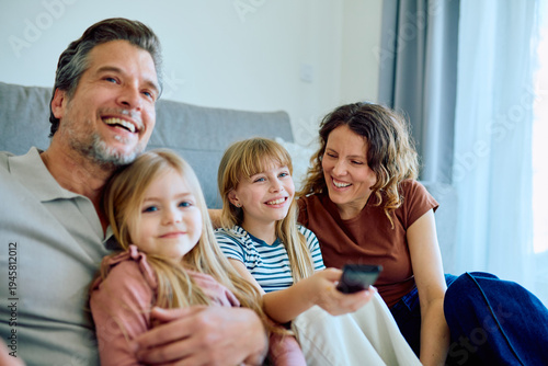 Smiling family of four enjoying entertainment together, laughing while sitting on the couch and spending quality time