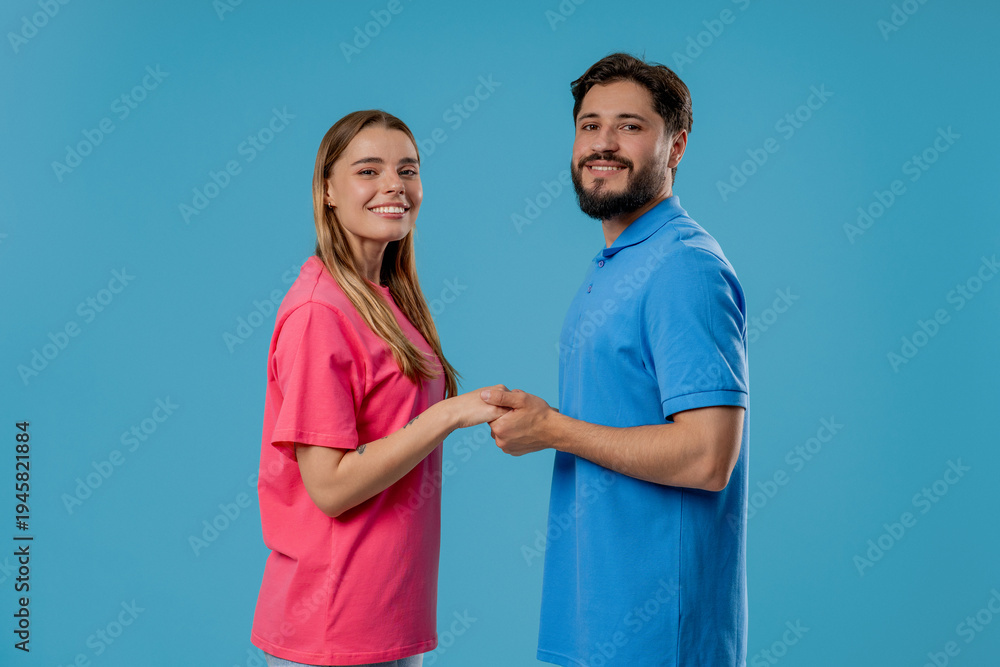Obraz premium Happy couple stands on blue, holding hands, look into camera. Romantic feelings.