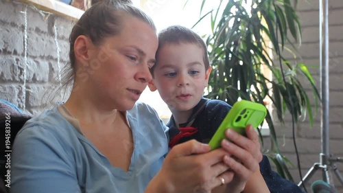 Mother and son, a small child, are sitting on the sofa looking at the phone