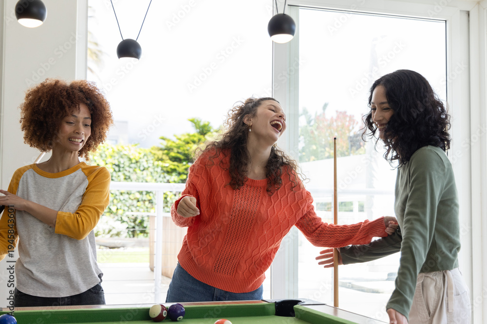 Fototapeta premium Diverse female friends laughing, playing at green pool table in game room with cue stick, balls