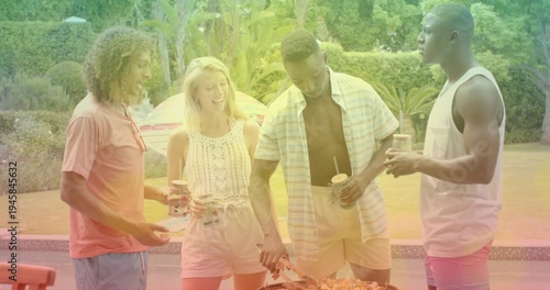 Grilling four friends in summer clothes tending portable grill on poolside patio, holding drinks