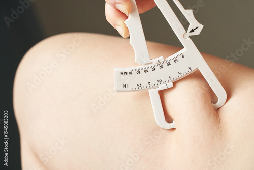 Female hand using skinfold caliper on arm for body fat measurement and fitness assessment.