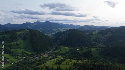 Aerial view of green mountain valley with forest hills and distant peaks under clouds