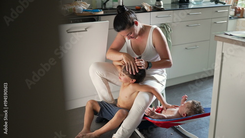 Foto Mother checking older child’s hair for lice while baby relaxes in rocker, everyd