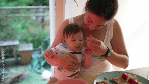Photos Mother feeding baby first solid food, baby biting vegetable, early food explorat