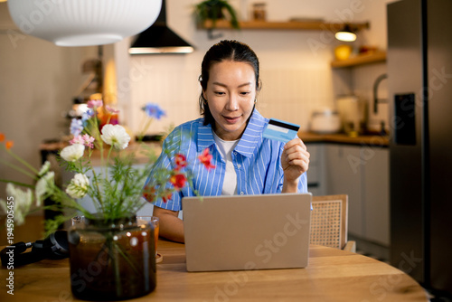 Woman shopping online with a credit card at home in a modern kitchen setting